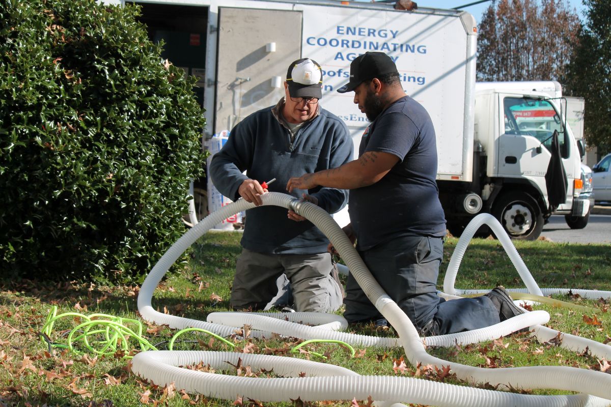 Two workers outside a building prepare ducting.