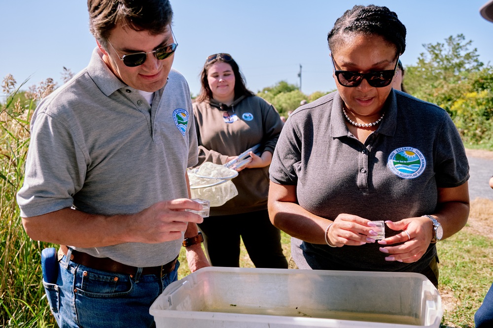 A man and woman examine a tub of dirty water. Behind them, a woman holds nets.