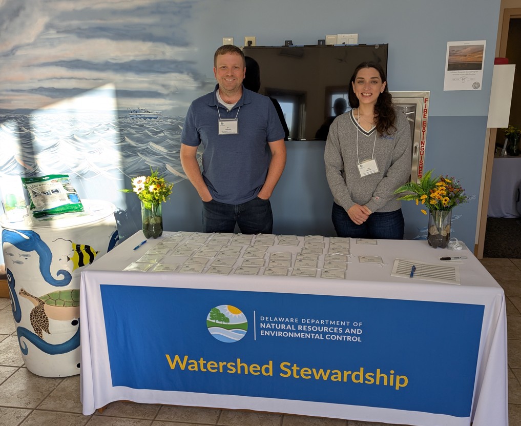 Two smiling staff members stand behind a registration table at a conference.