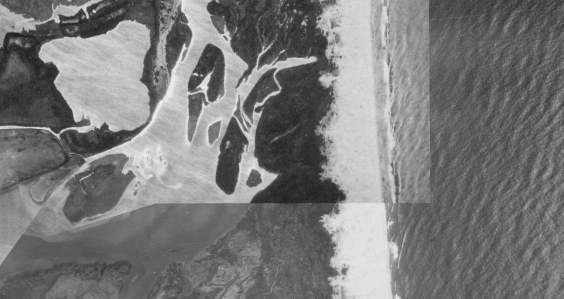 An aerial view, from historic photos, showing a barrier beach with the ocean on one side and shallow bays on the other.