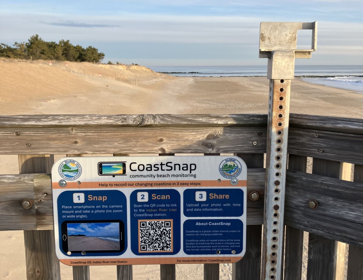 Looking out at a beach from a viewing platform with a metal pole holding a camera mount and instructions on how to take a "Coast Snap" photo.
