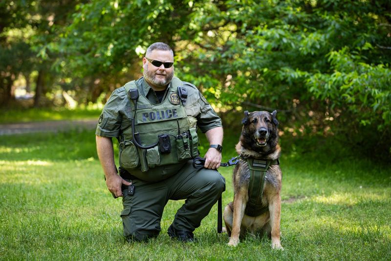 A law enforcement officer kneels alongside a police German shepherd.