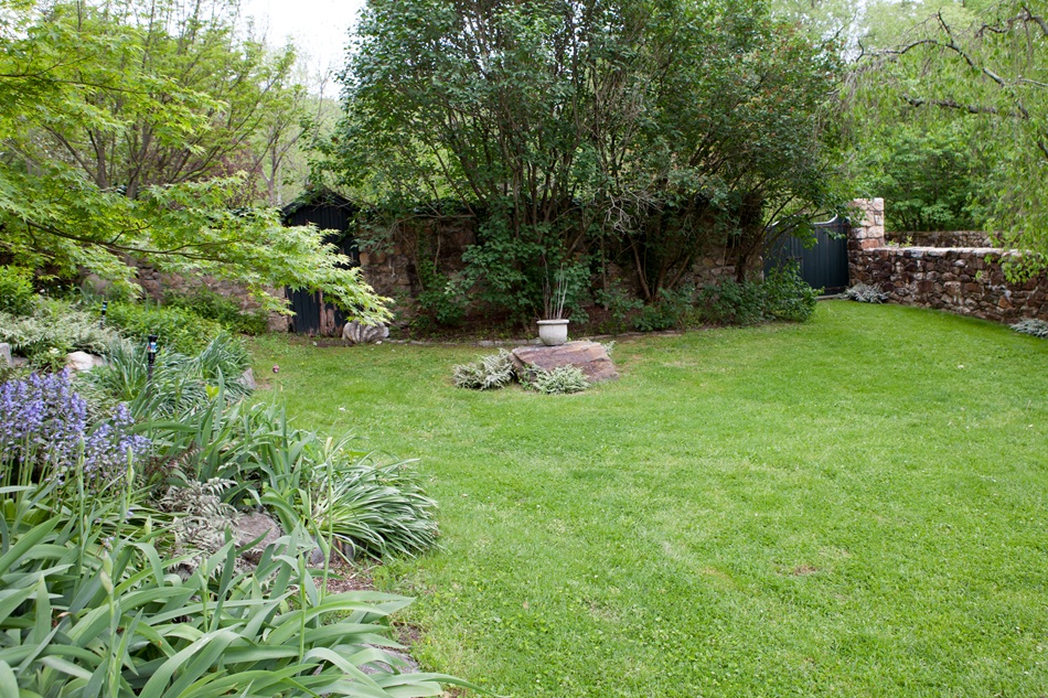 Stone walls and flora are pictured around a green lawn.