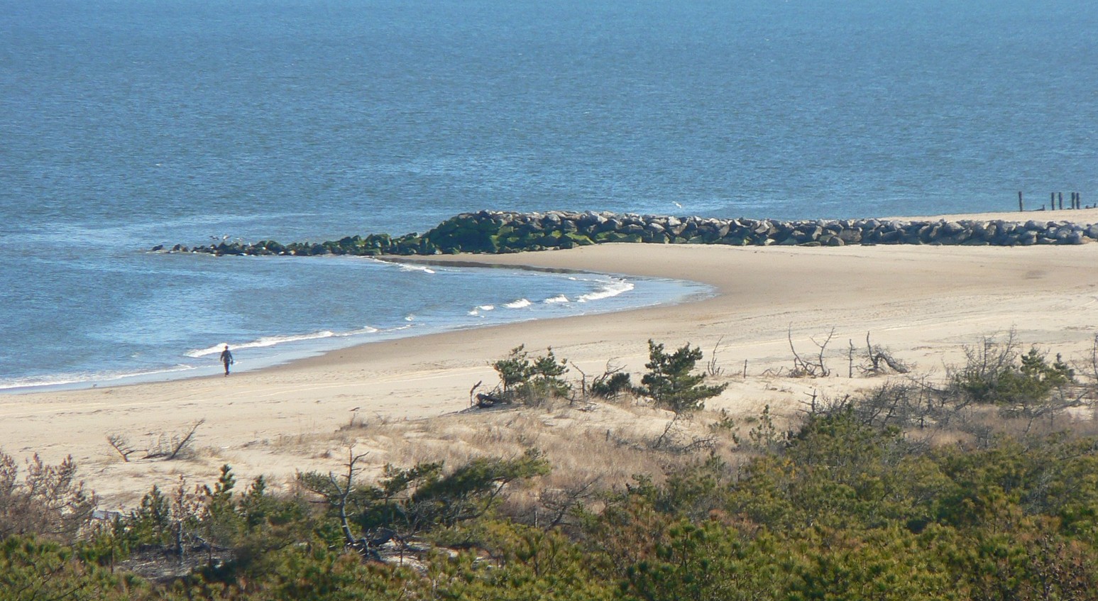A lone person walks along the waterline on a sandy beach.