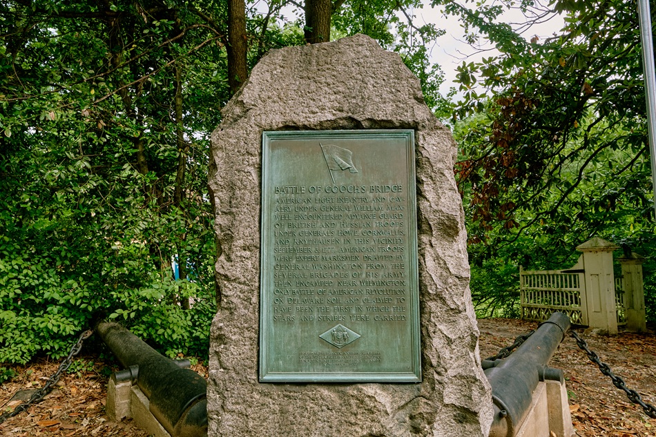 A plaque in a rock details the Battle of Cooch's Bridge, while two cannons sit next to it.