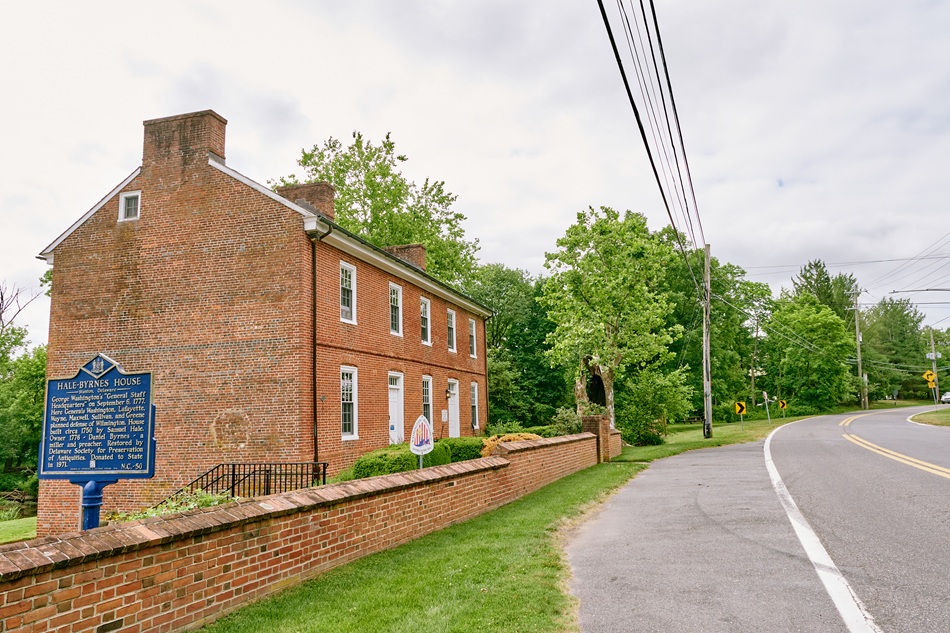 A brick house with a brick wall in front sits next to a road.