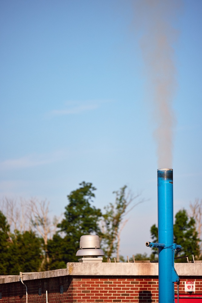A plume of smoke releases into the sky from a blue pipe.
